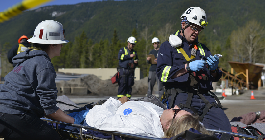 Emergency responders assist a person on a stretcher during a training exercise in a mountainous area.